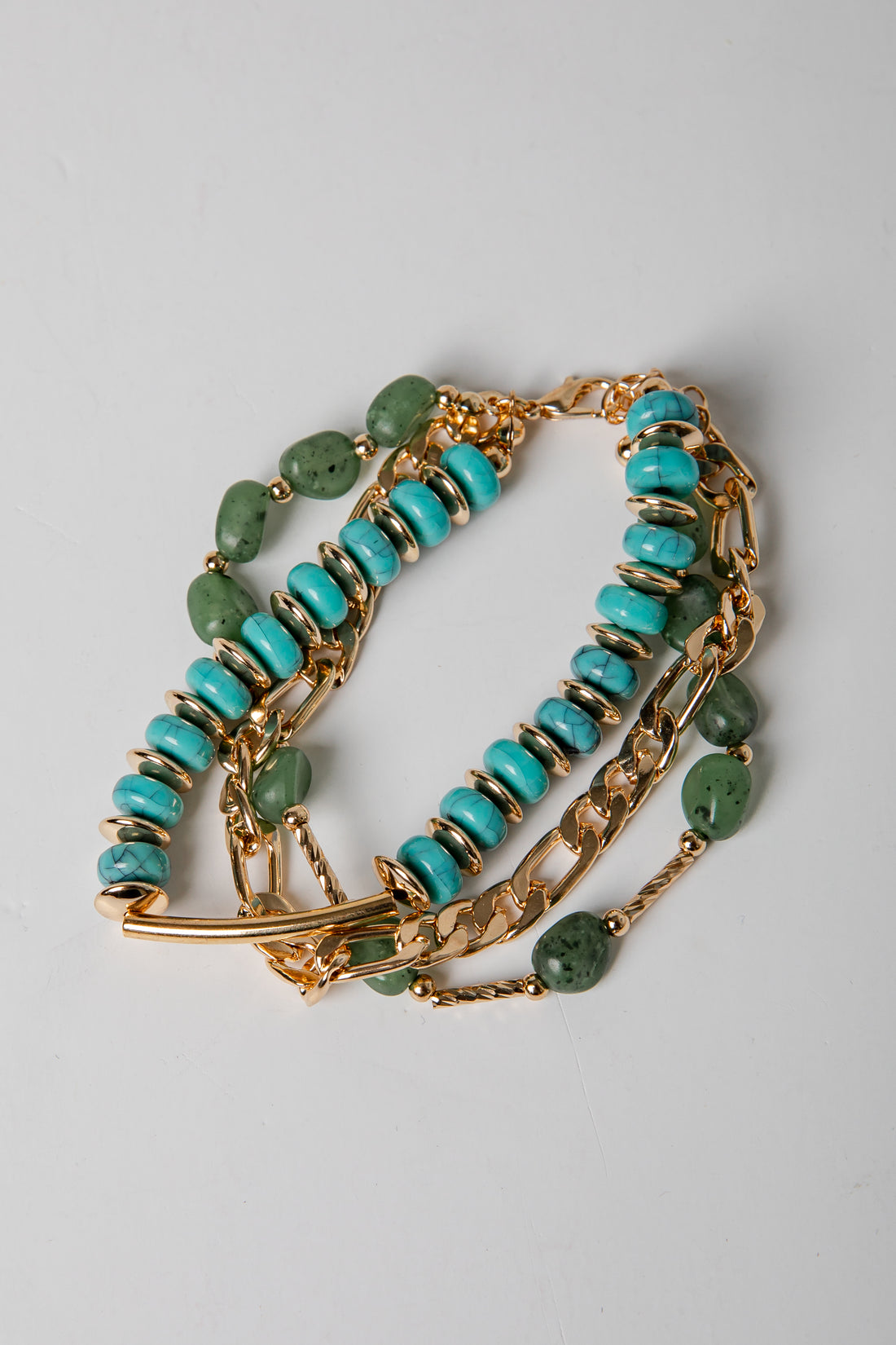 Gold bracelet with turquoise and green beads on a light gray background