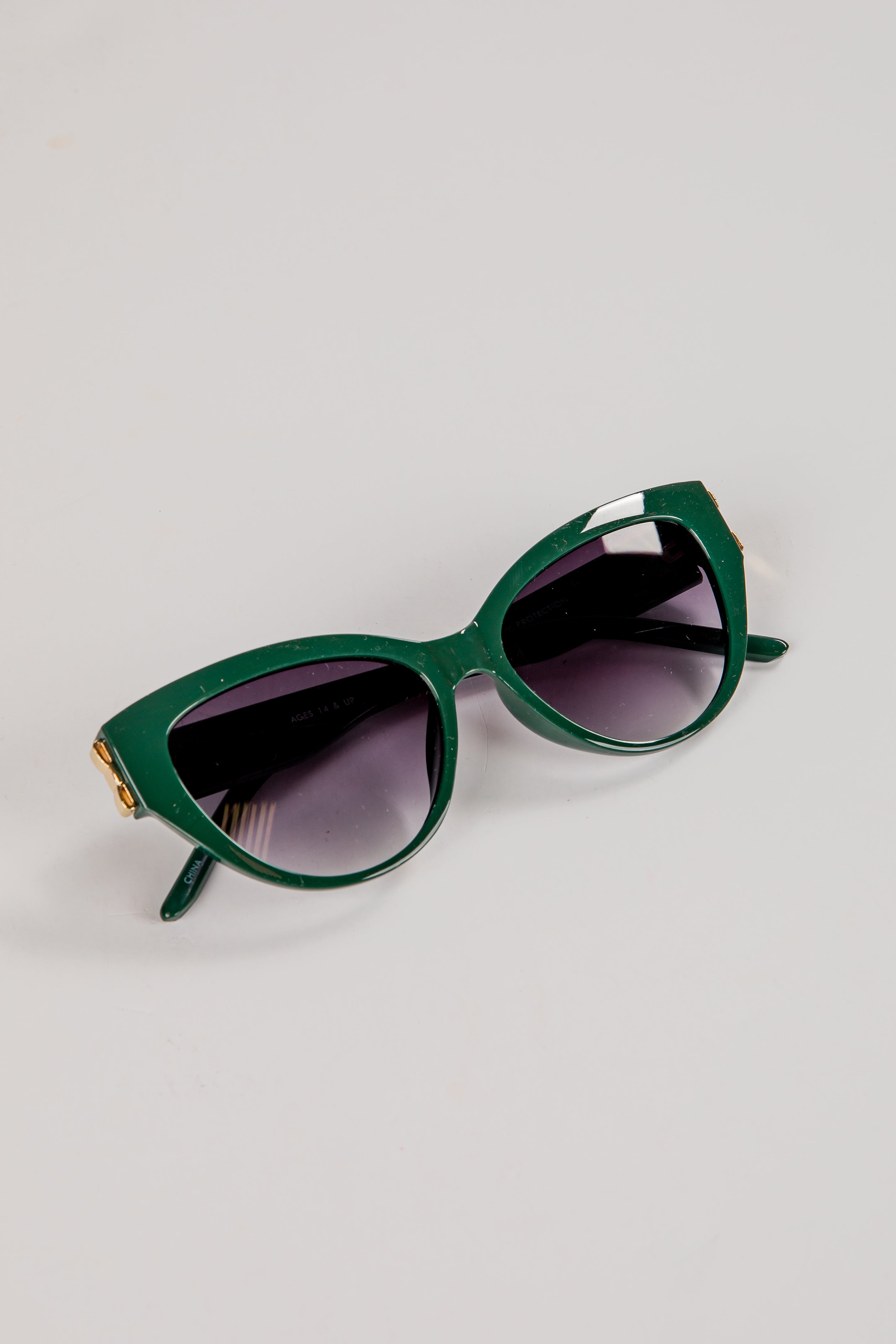 Green sunglasses with dark lenses on a light gray background