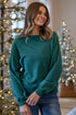 Woman wearing a teal sweater standing in front of Christmas trees.
