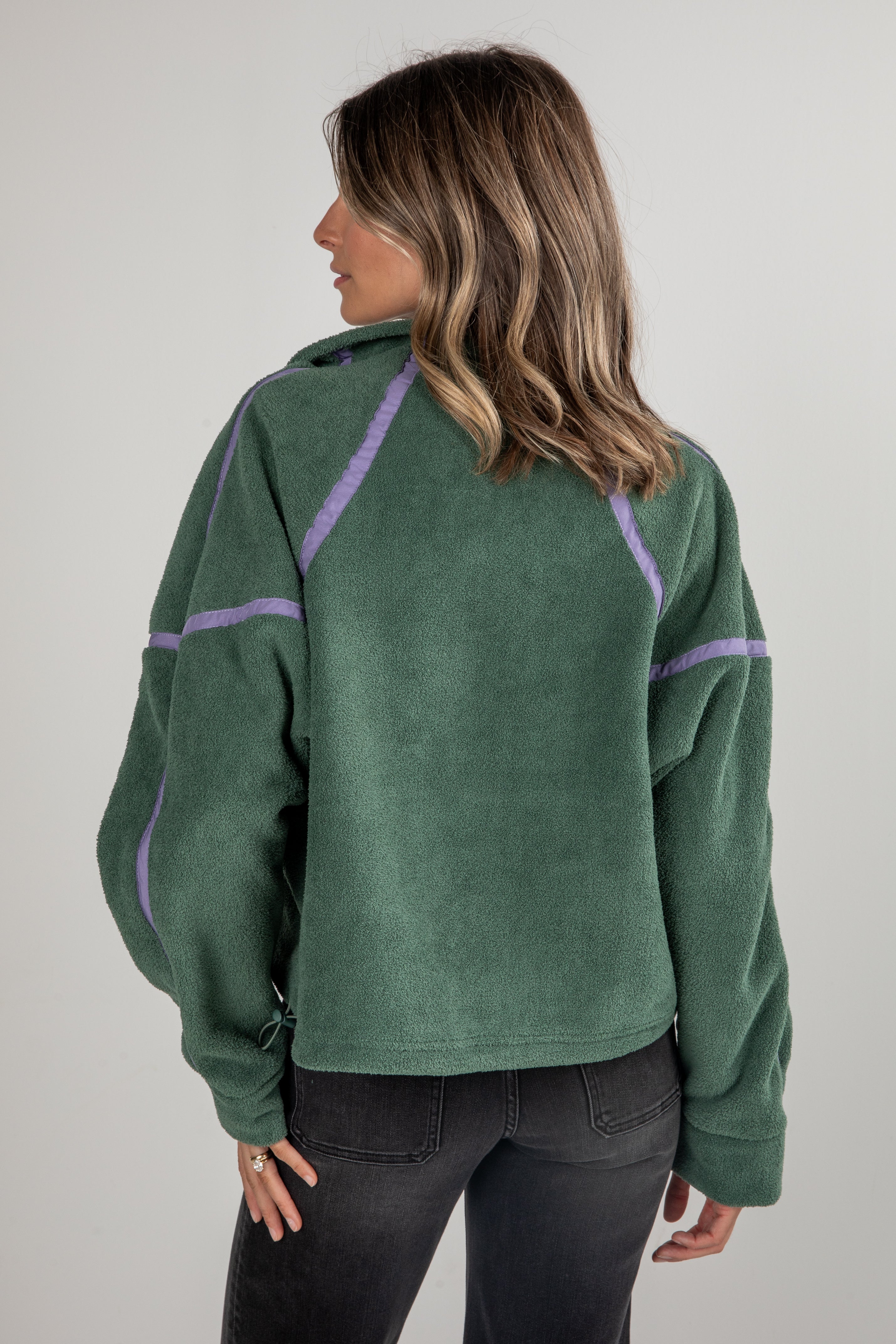 Person wearing a green fleece pullover with purple accents on a plain background