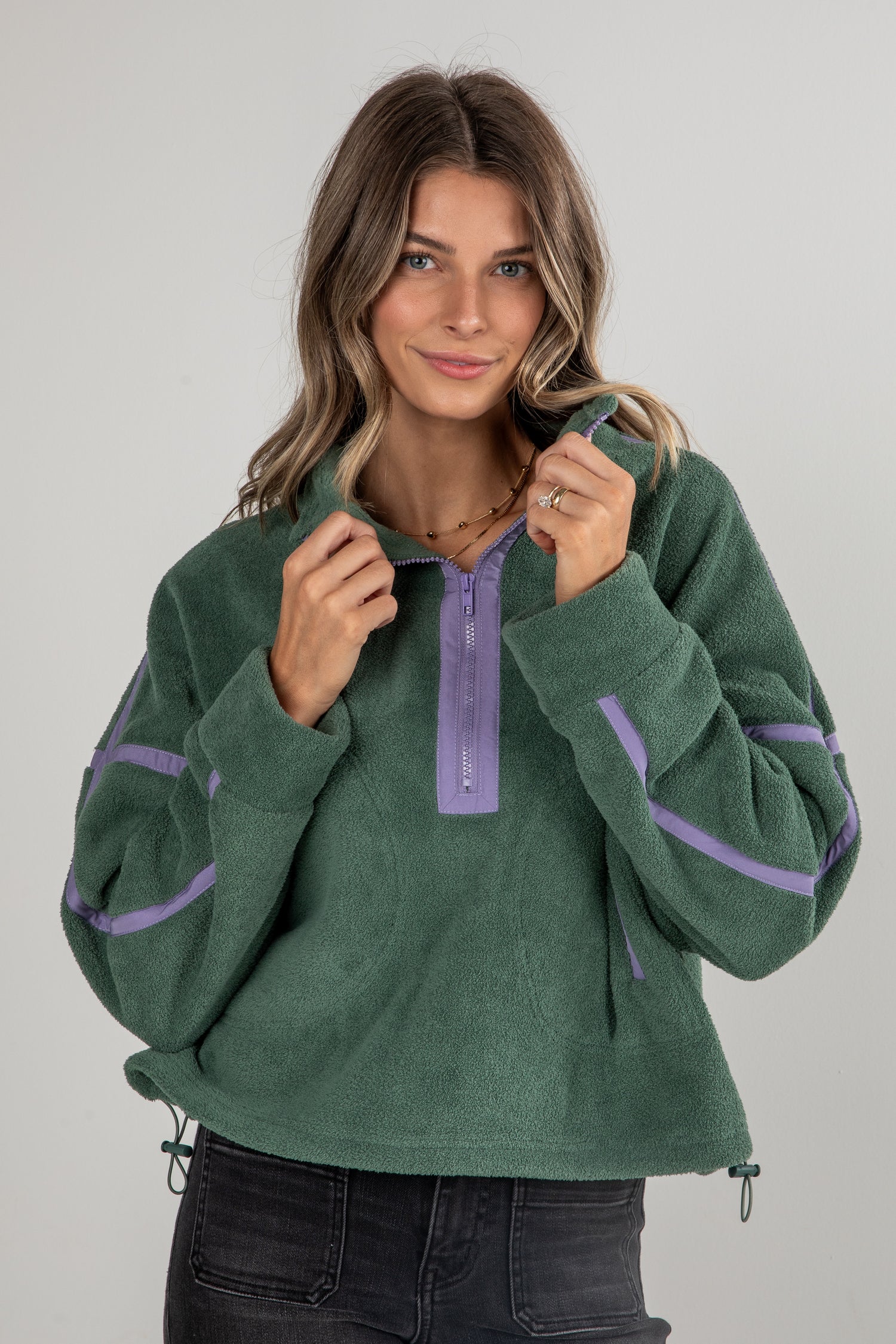Woman wearing a green fleece pullover with purple accents on a gray background