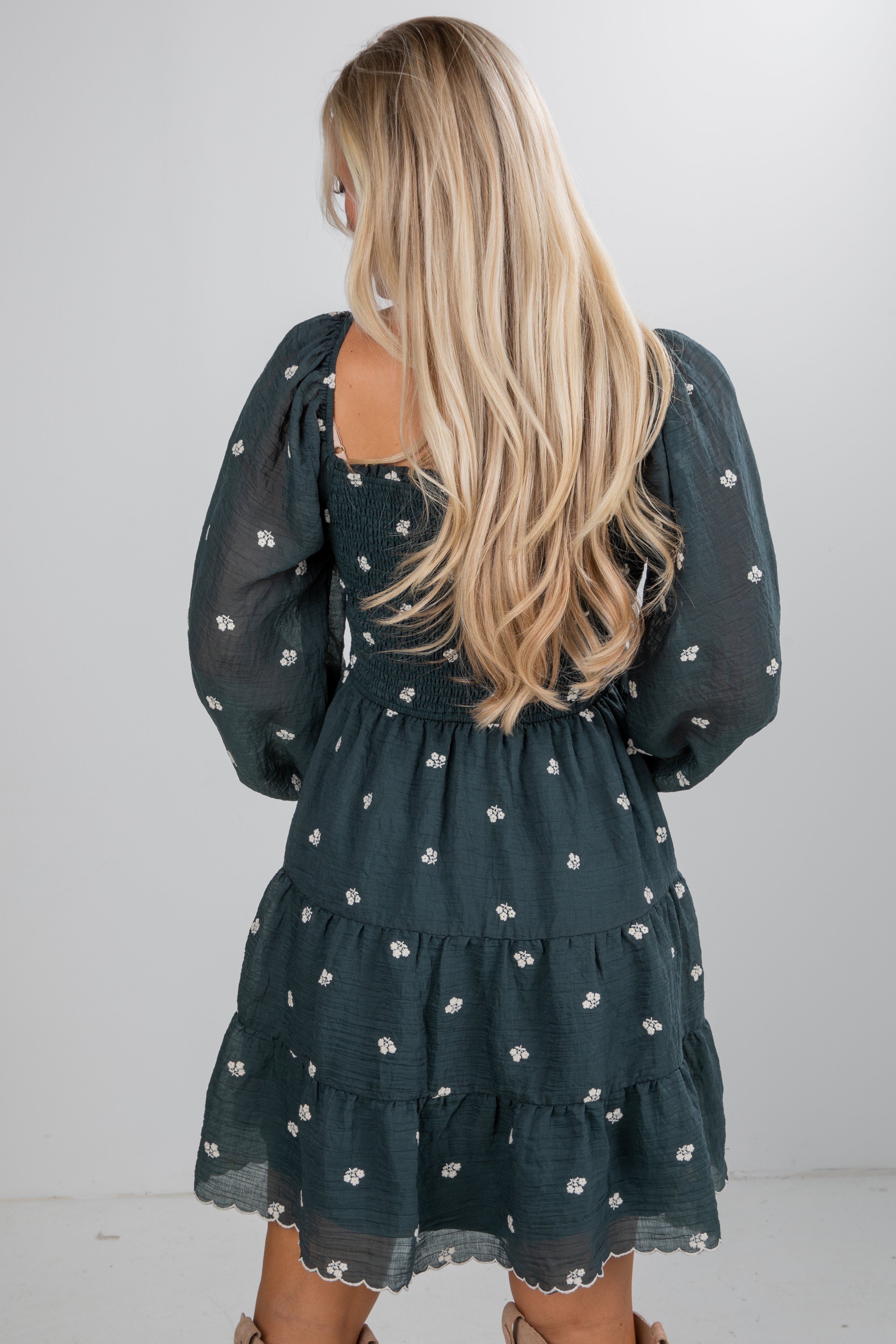 Woman wearing a dark green dress with floral patterns, standing against a plain background