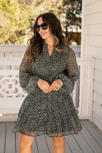 Woman wearing a black floral dress on a wooden deck with trees in the background