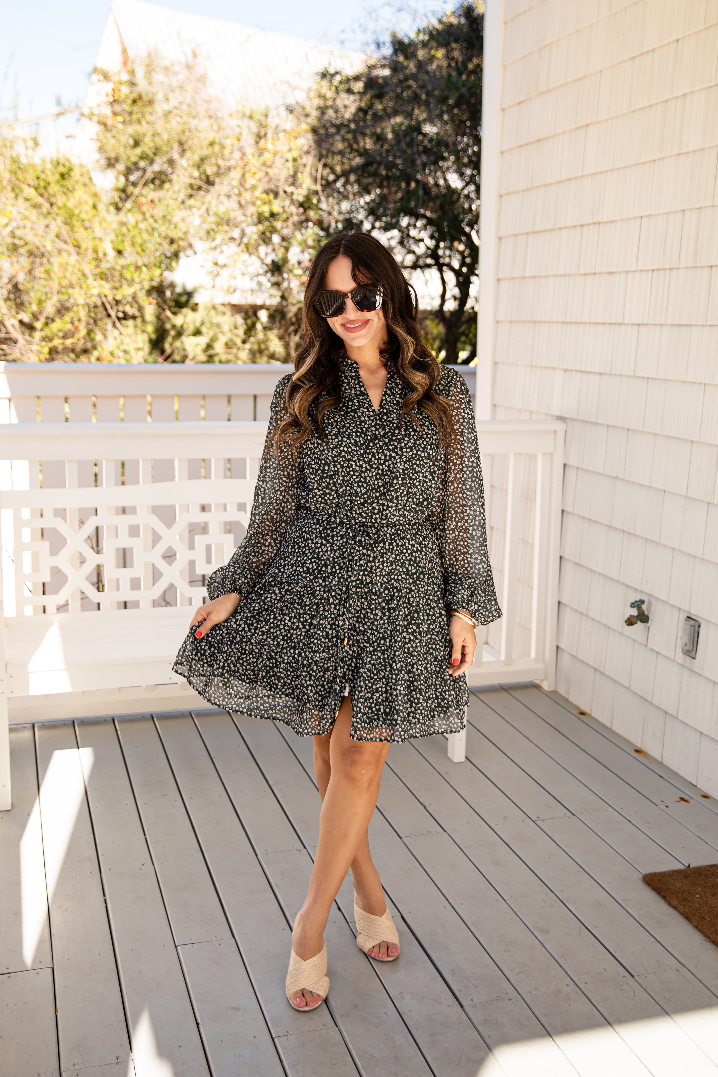 Woman in a patterned dress standing on a wooden deck with trees in the background