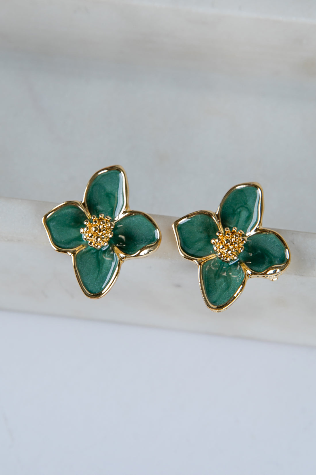 Green floral earrings with gold accents on a white marble surface