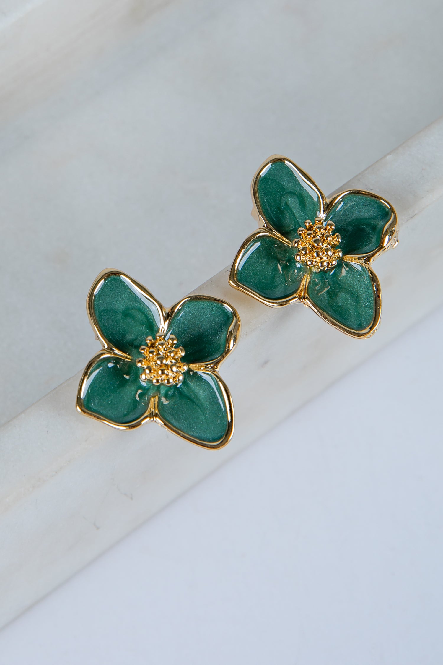 Green flower-shaped earrings with gold accents on a white surface