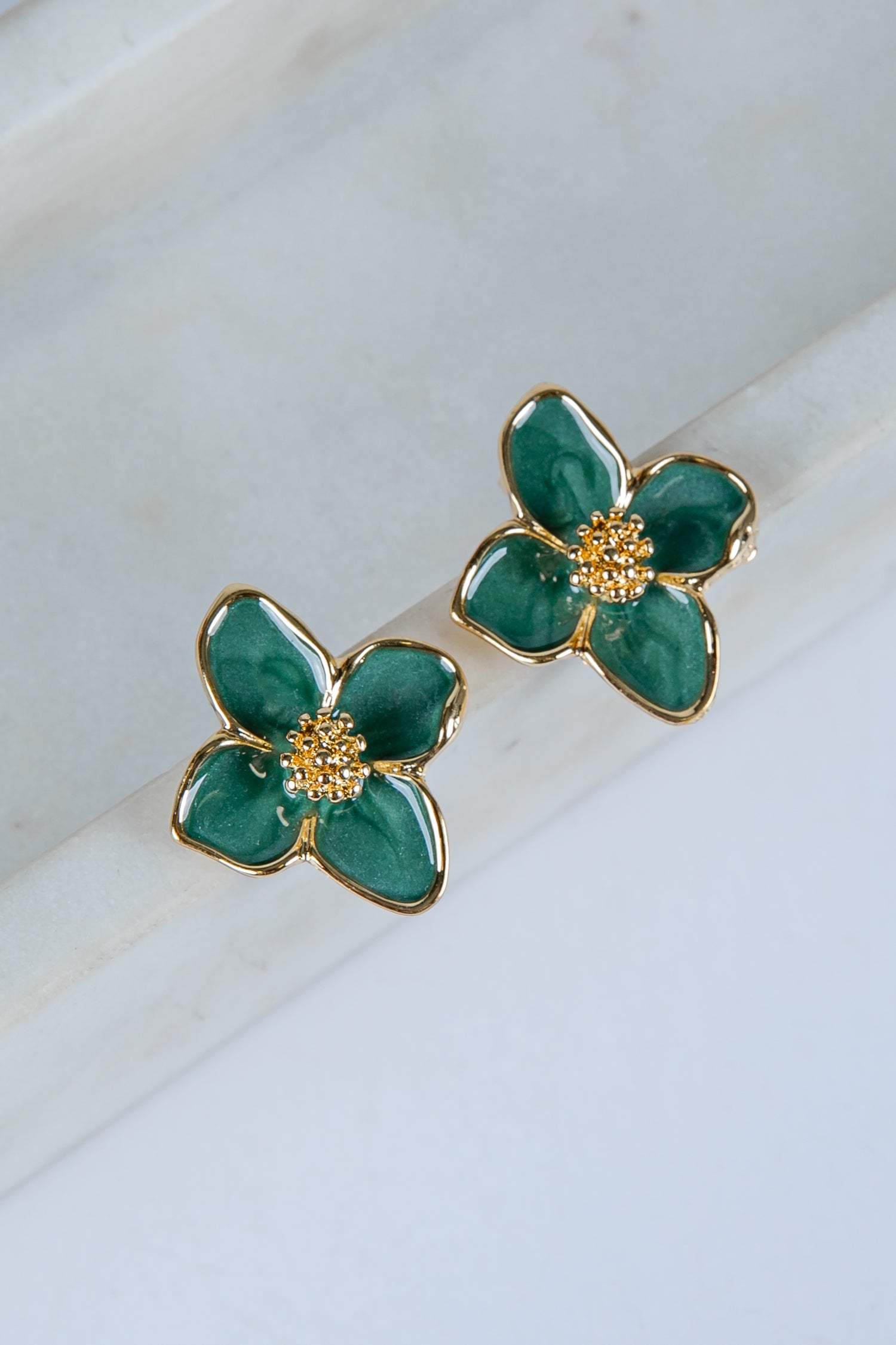 Green flower-shaped earrings with gold accents on a marble surface