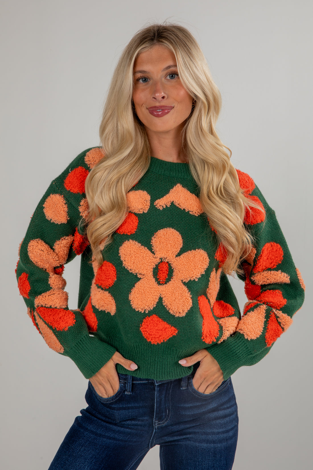 Woman wearing a green sweater with orange floral patterns on a gray background
