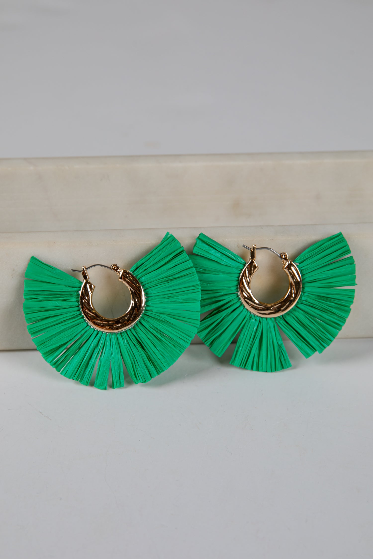 Green ruffled earrings with gold hoop centers on a light gray background