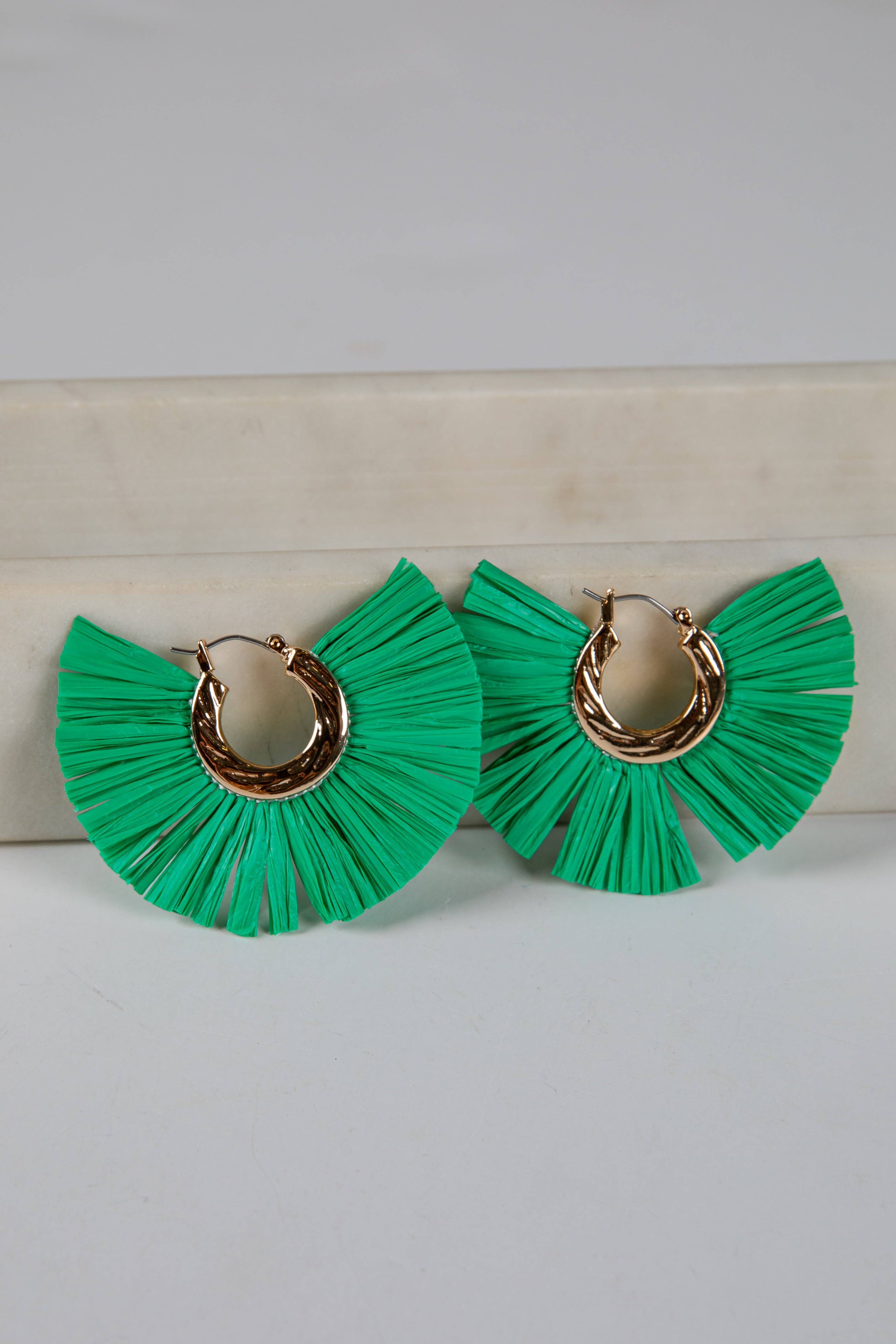 Green ruffled earrings with gold hoop centers on a light gray background