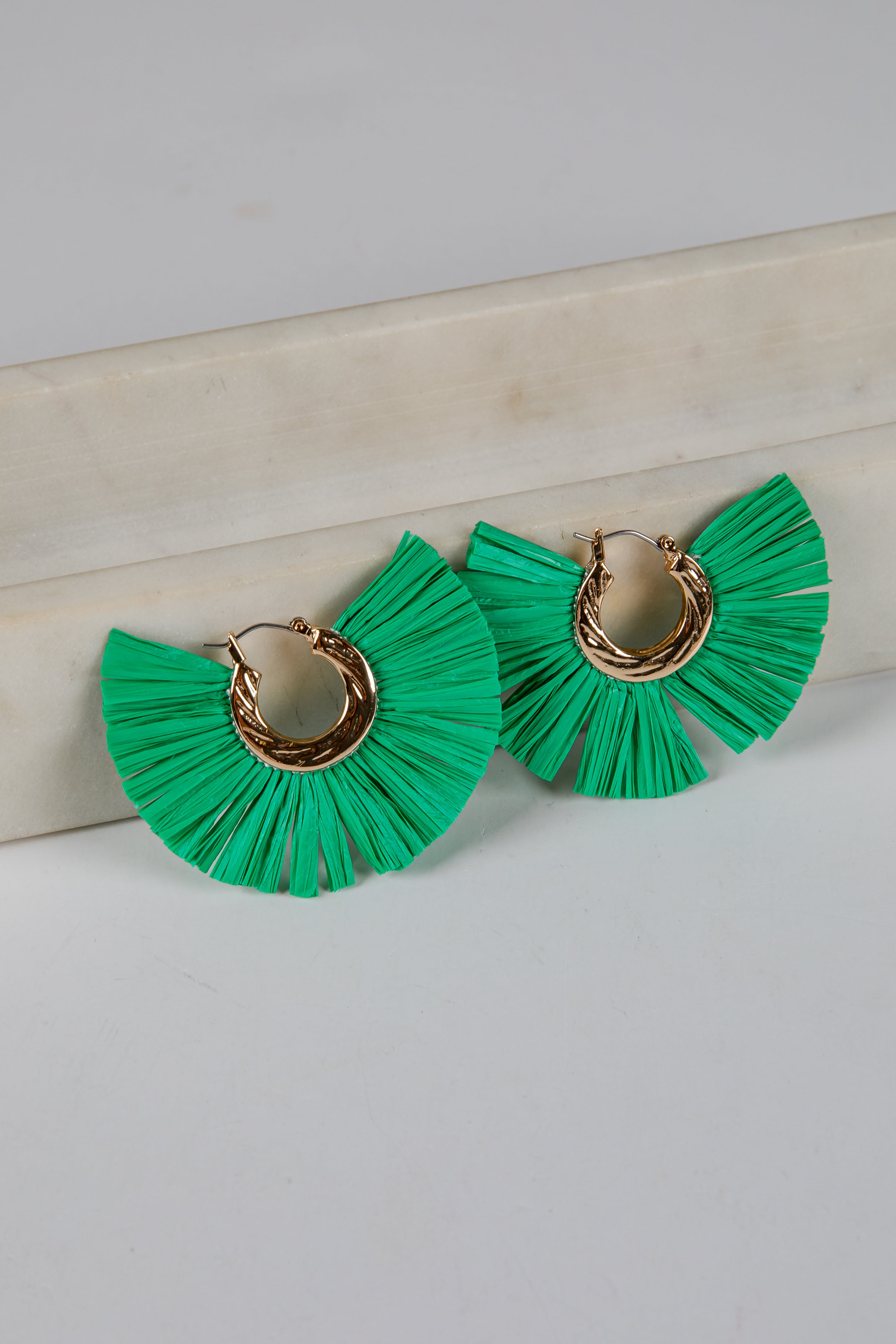 Green ruffled earrings with gold circular centers on a light gray background