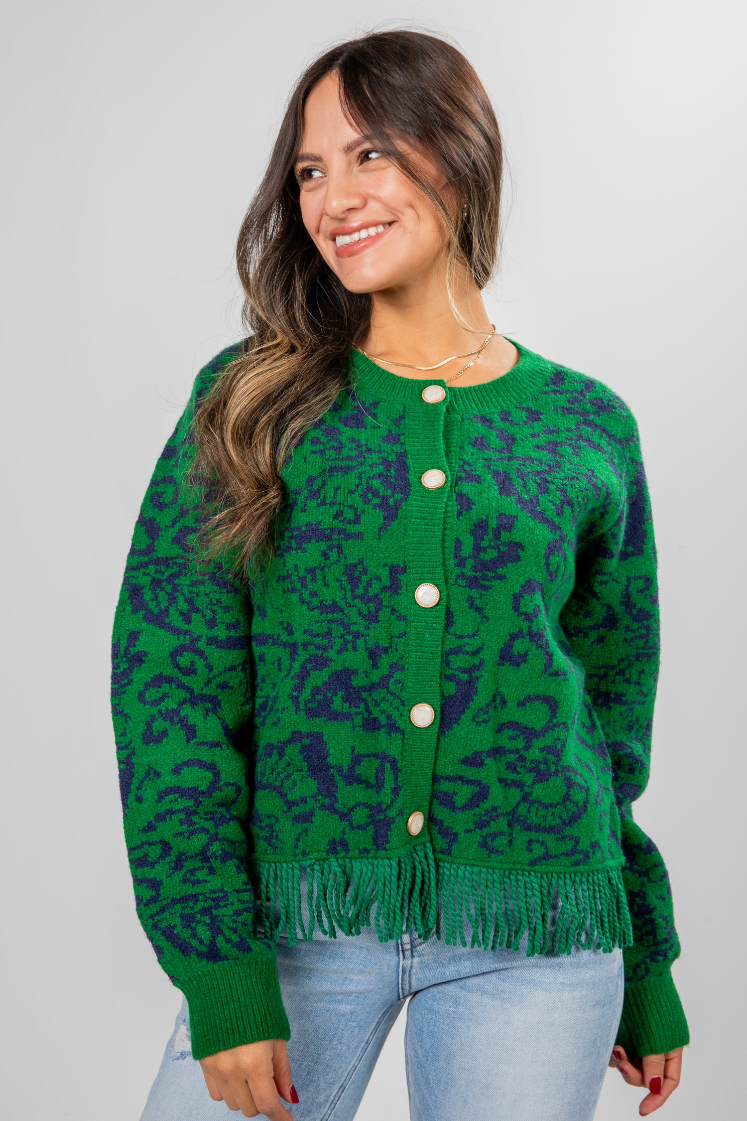 Woman wearing a green patterned cardigan with white buttons on a gray background