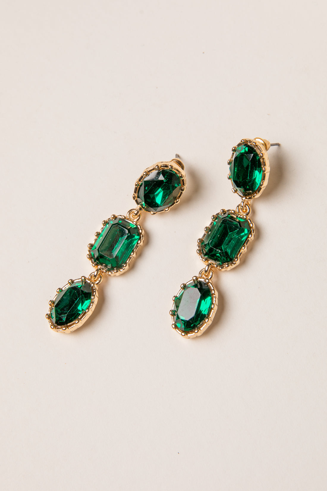 Green gemstone earrings with gold accents on a beige background