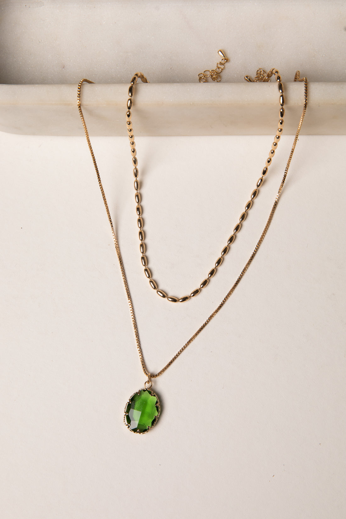 Two gold necklaces with green pendants on a white background