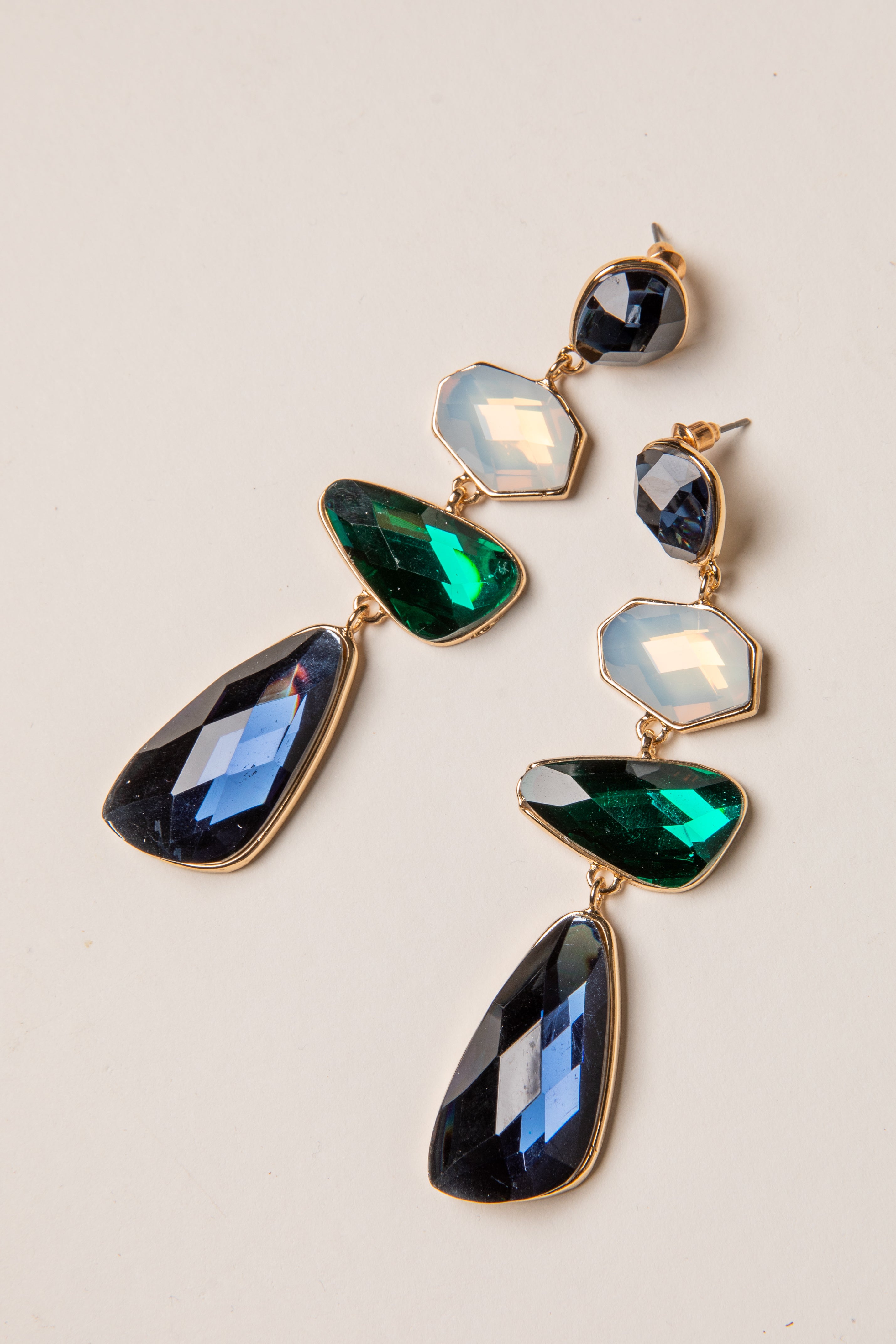 Pair of gold earrings with green and blue gemstones on a light background