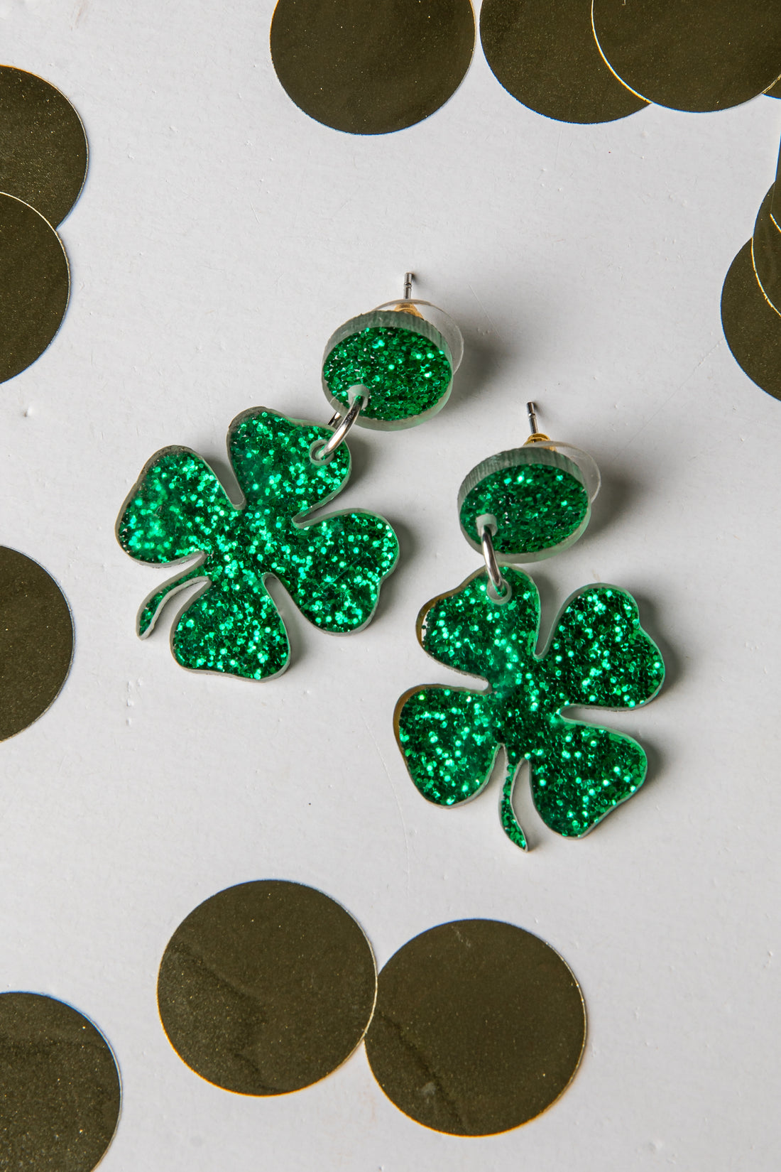 Green glittery shamrock earrings on a white background with gold coins.