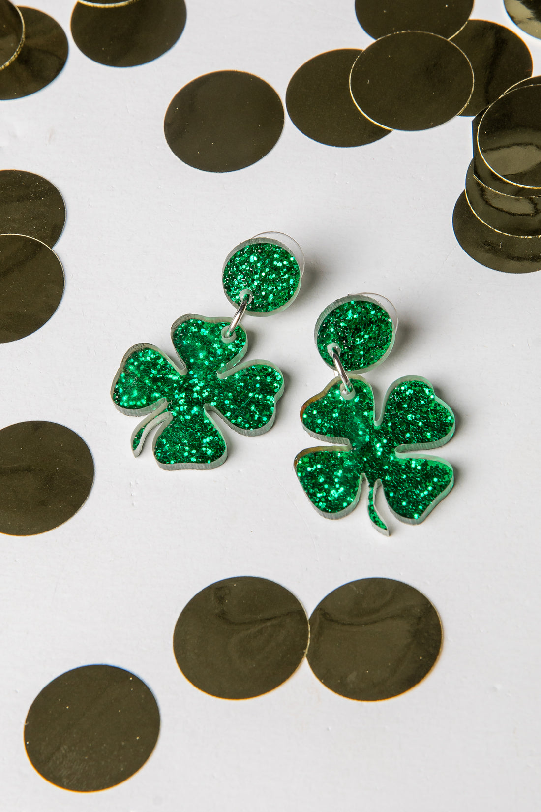 Green glitter shamrock earrings on a white background with gold coins.