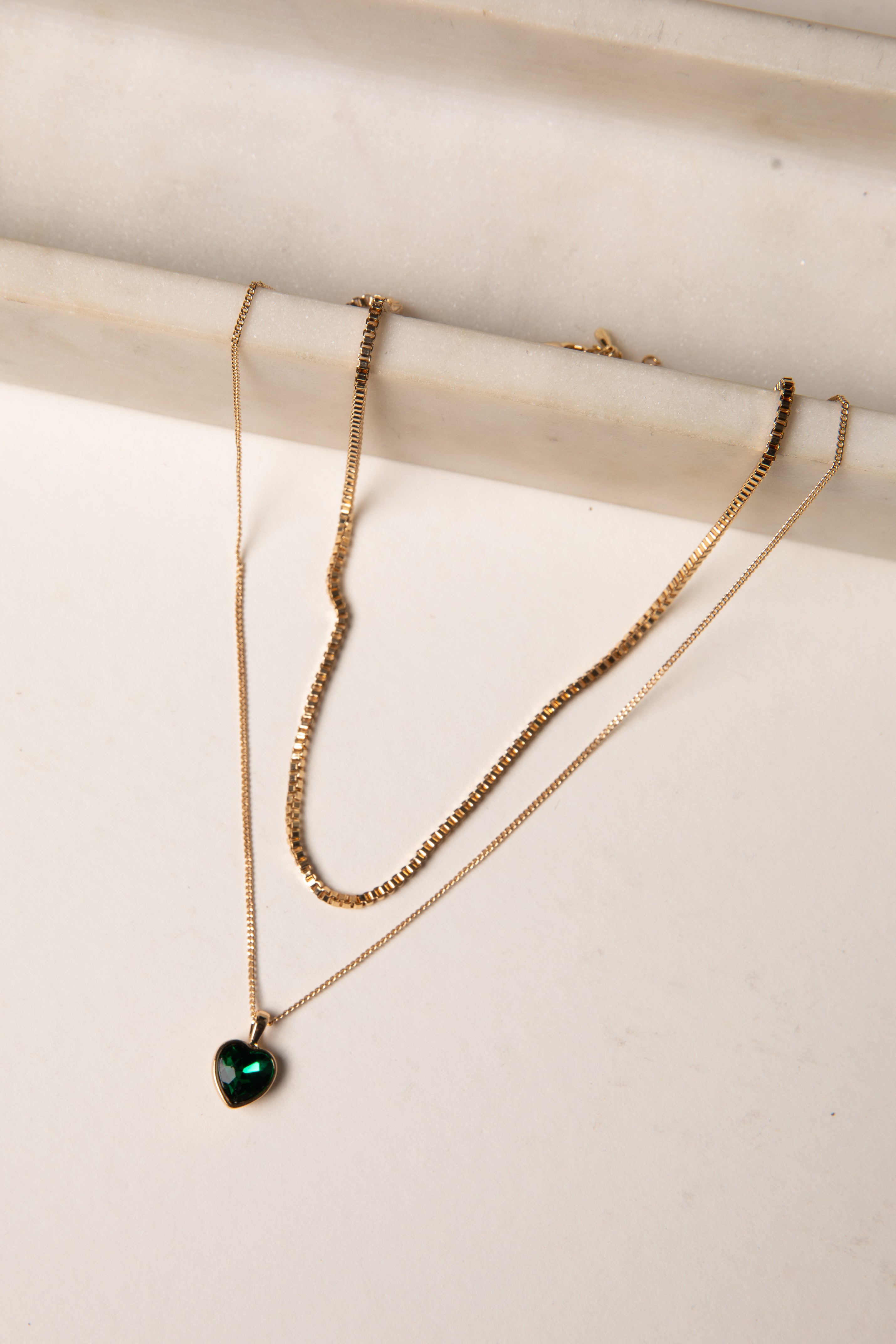 Gold necklace with a heart-shaped green gemstone on a white surface