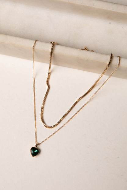 Gold necklace with a heart-shaped green gemstone on a white surface