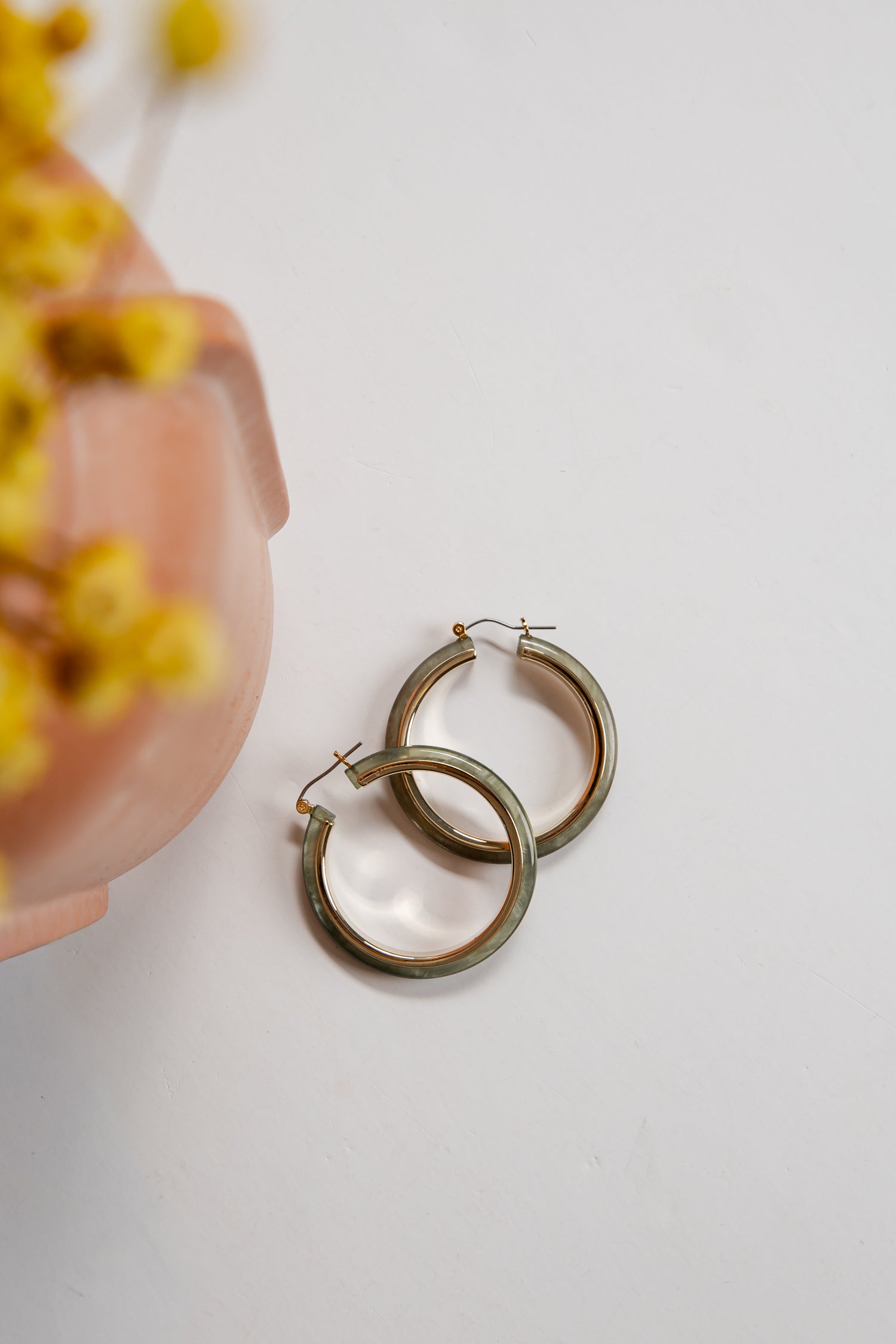 Gold hoop earrings on a light surface with blurred yellow flowers in the background