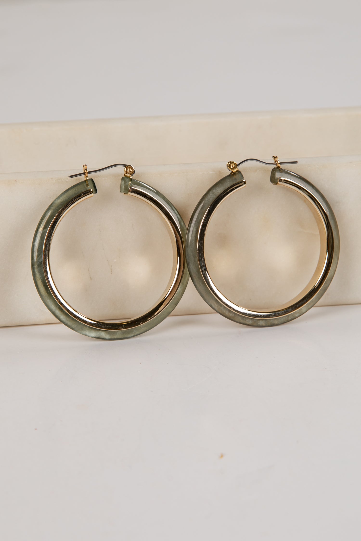 Gold hoop earrings on a white cushion with a light gray background