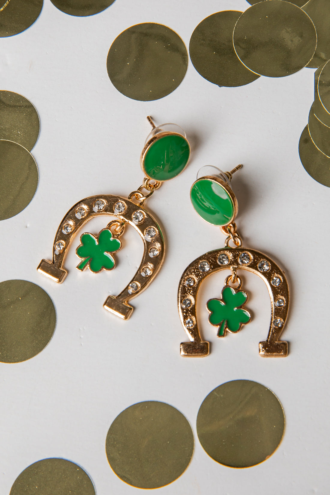 Gold horseshoe earrings with green clover leaves on a white background with gold coins.