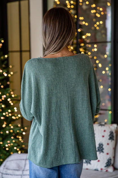 Person wearing a green sweater in front of a decorated Christmas tree with lights.
