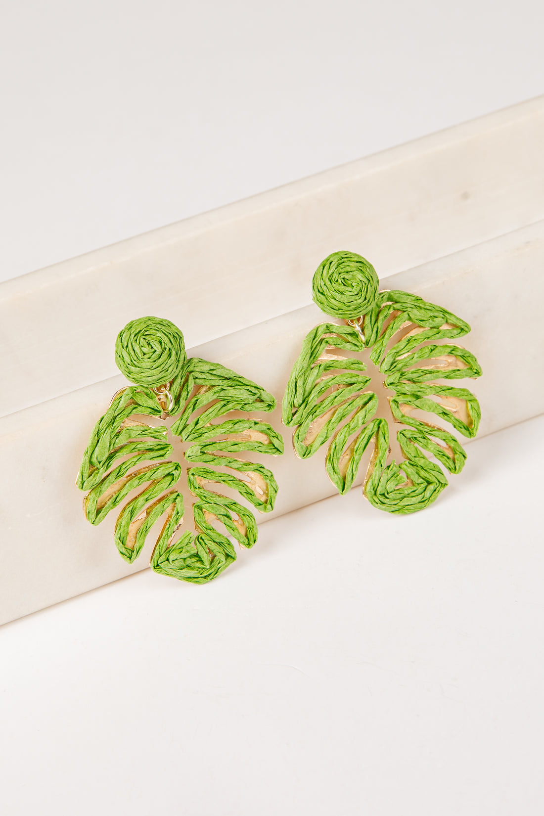 Green leaf-shaped earrings on a white surface