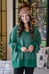 Woman wearing a green sweater and brown beanie standing in a room with Christmas decorations.