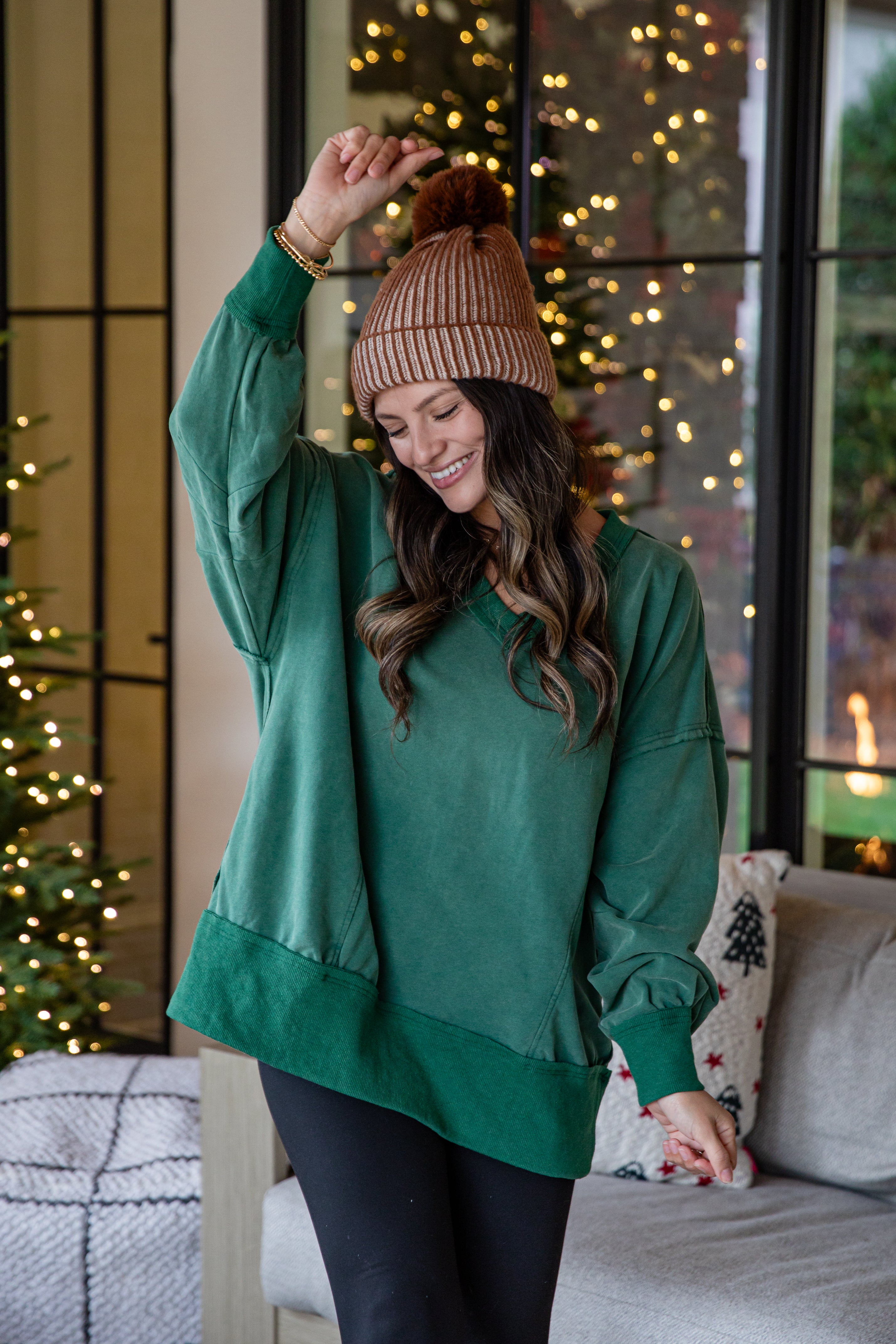 Woman wearing a green sweater and brown beanie indoors with festive decorations.