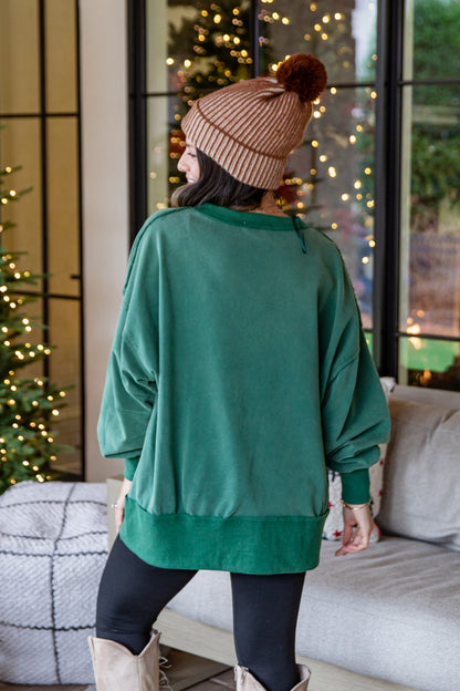 Person wearing a green sweater and brown beanie in a cozy living room with Christmas decorations.