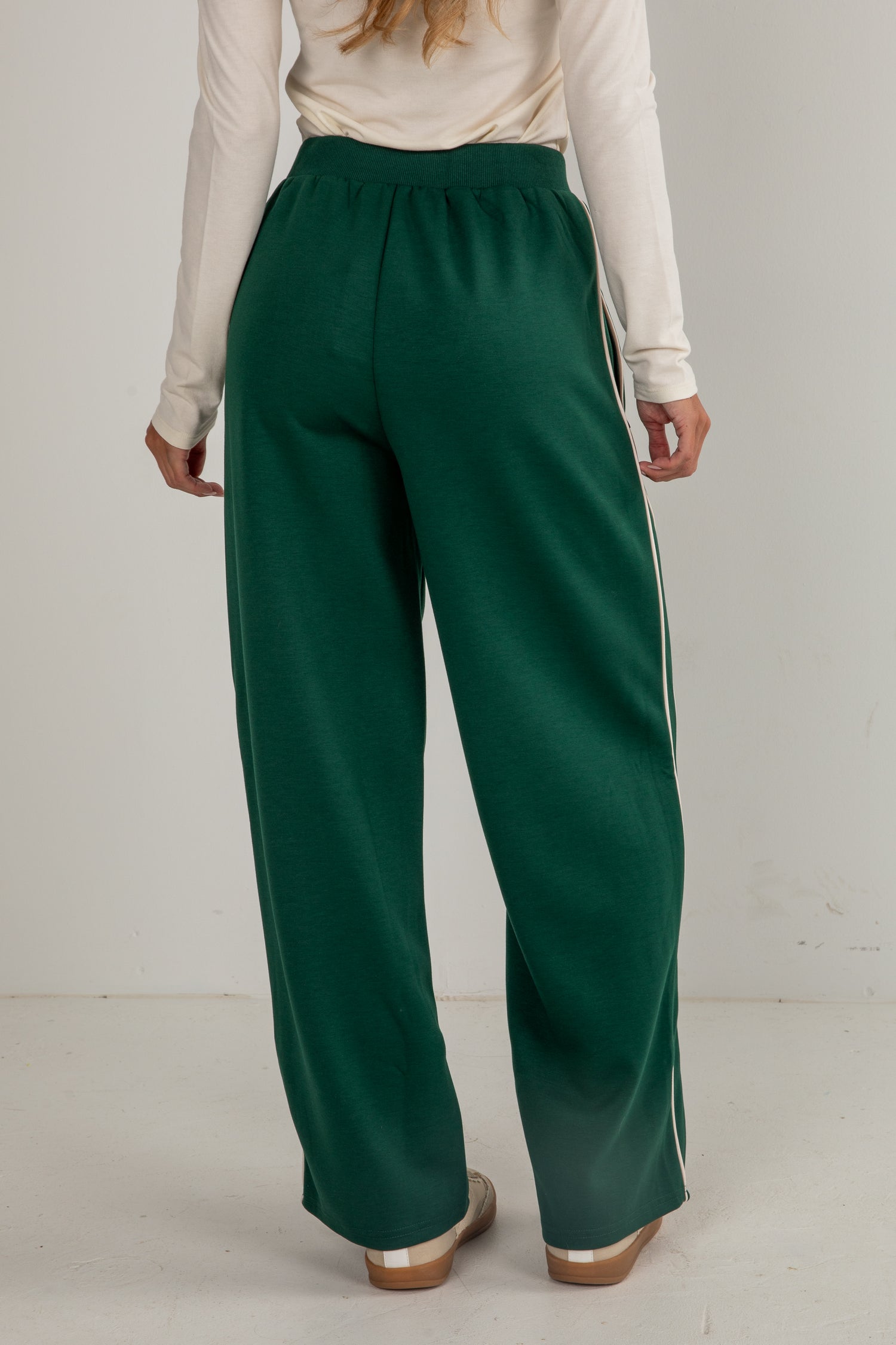 Person wearing green wide-leg pants and a cream top on a white background
