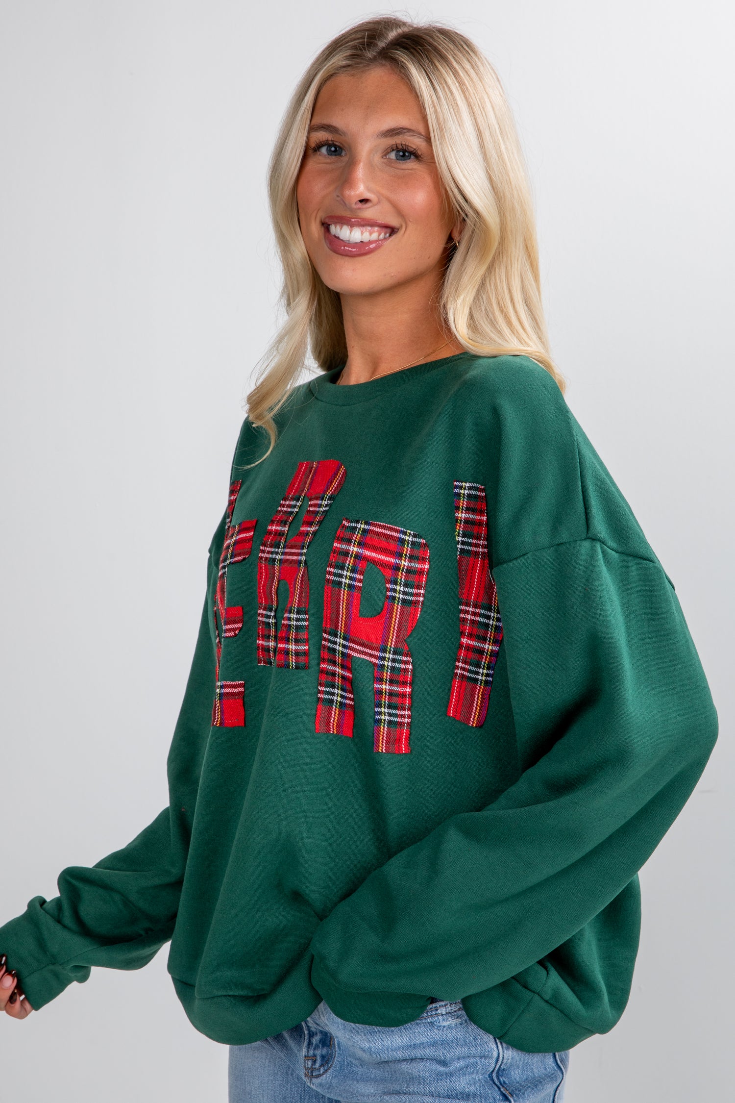 Woman wearing a green sweatshirt with red plaid text on a plain background