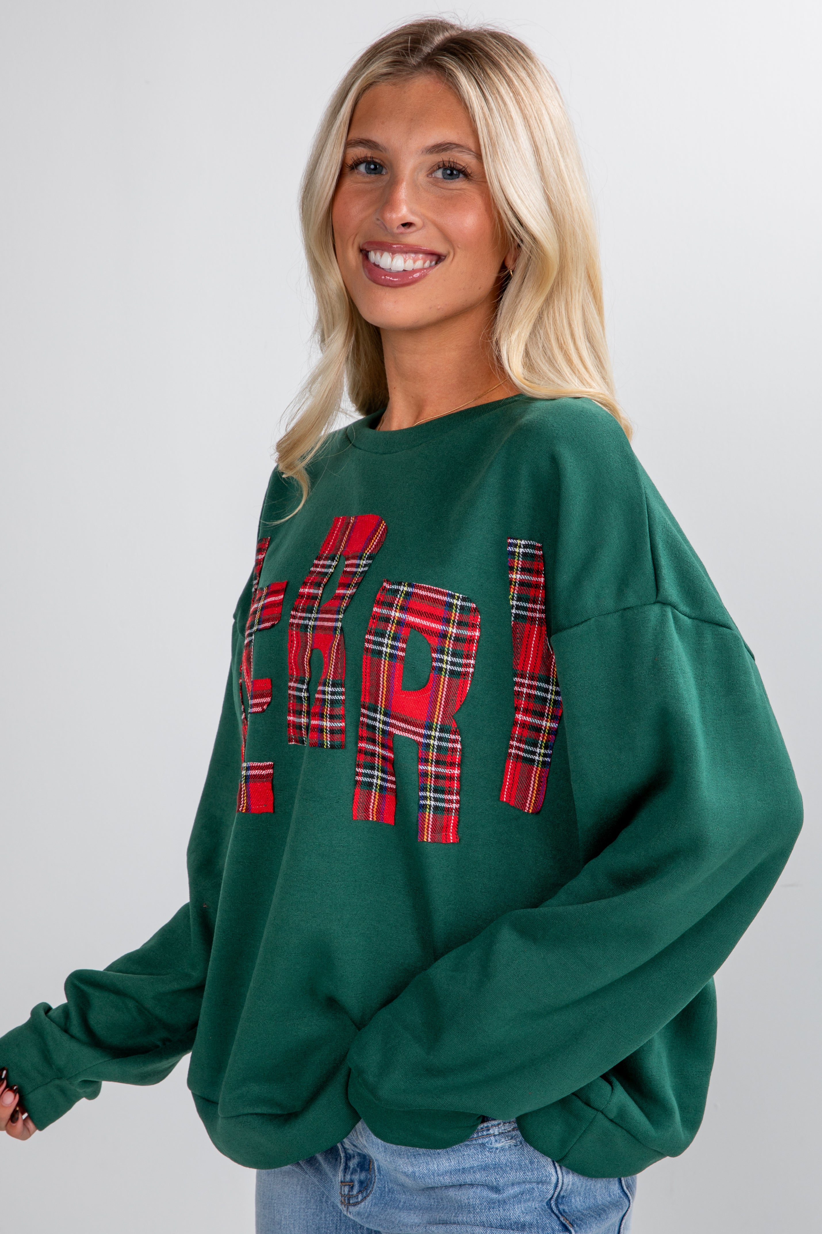Woman wearing a green sweatshirt with red plaid text on a plain background