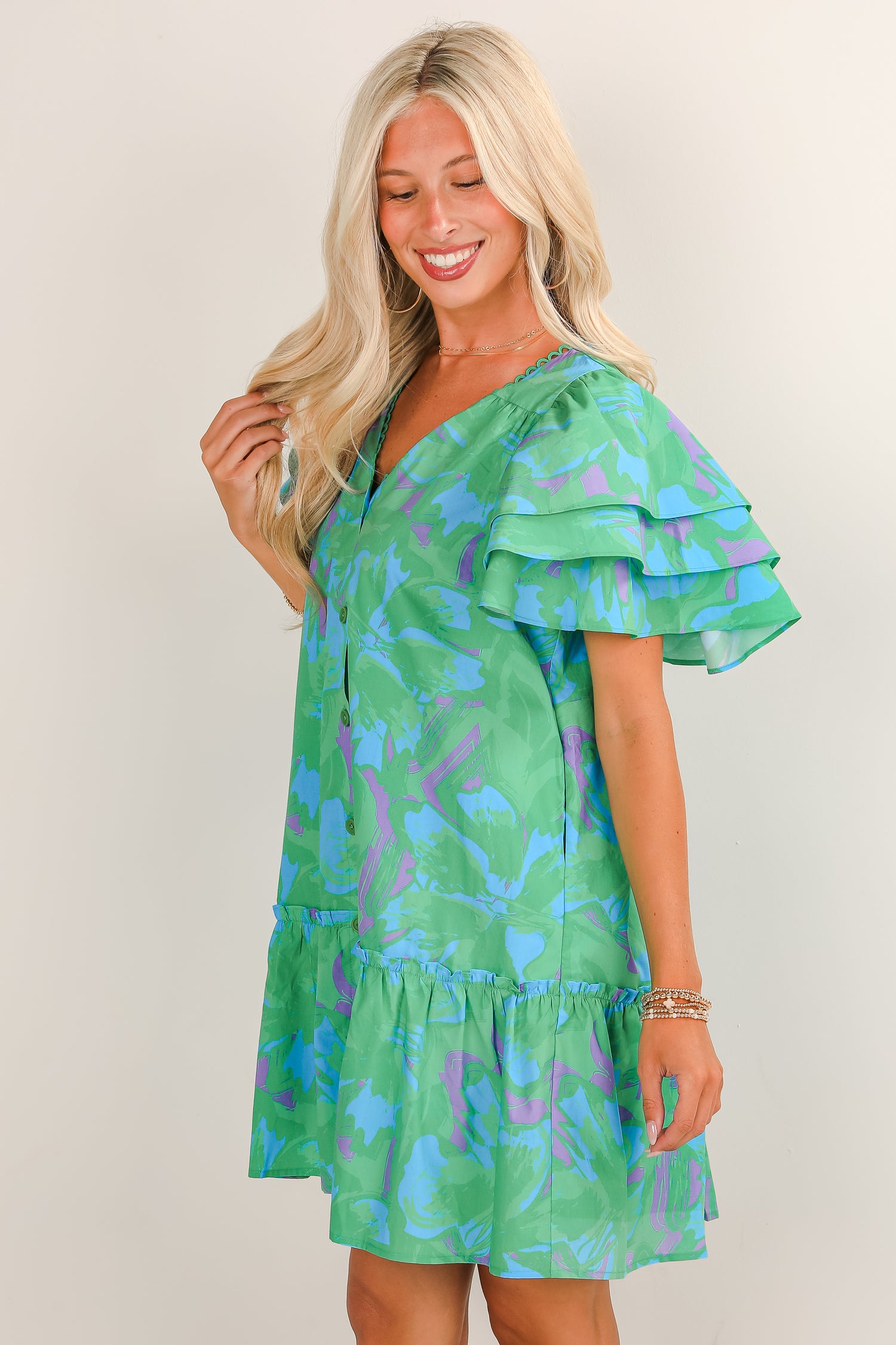 Woman wearing a green dress with blue floral pattern on a plain background