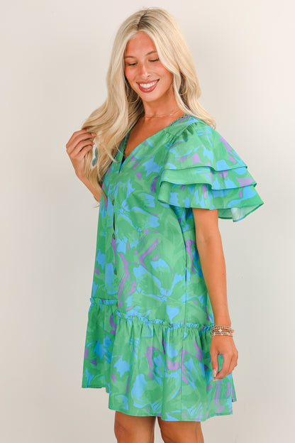 Woman wearing a green dress with blue floral pattern on a plain background