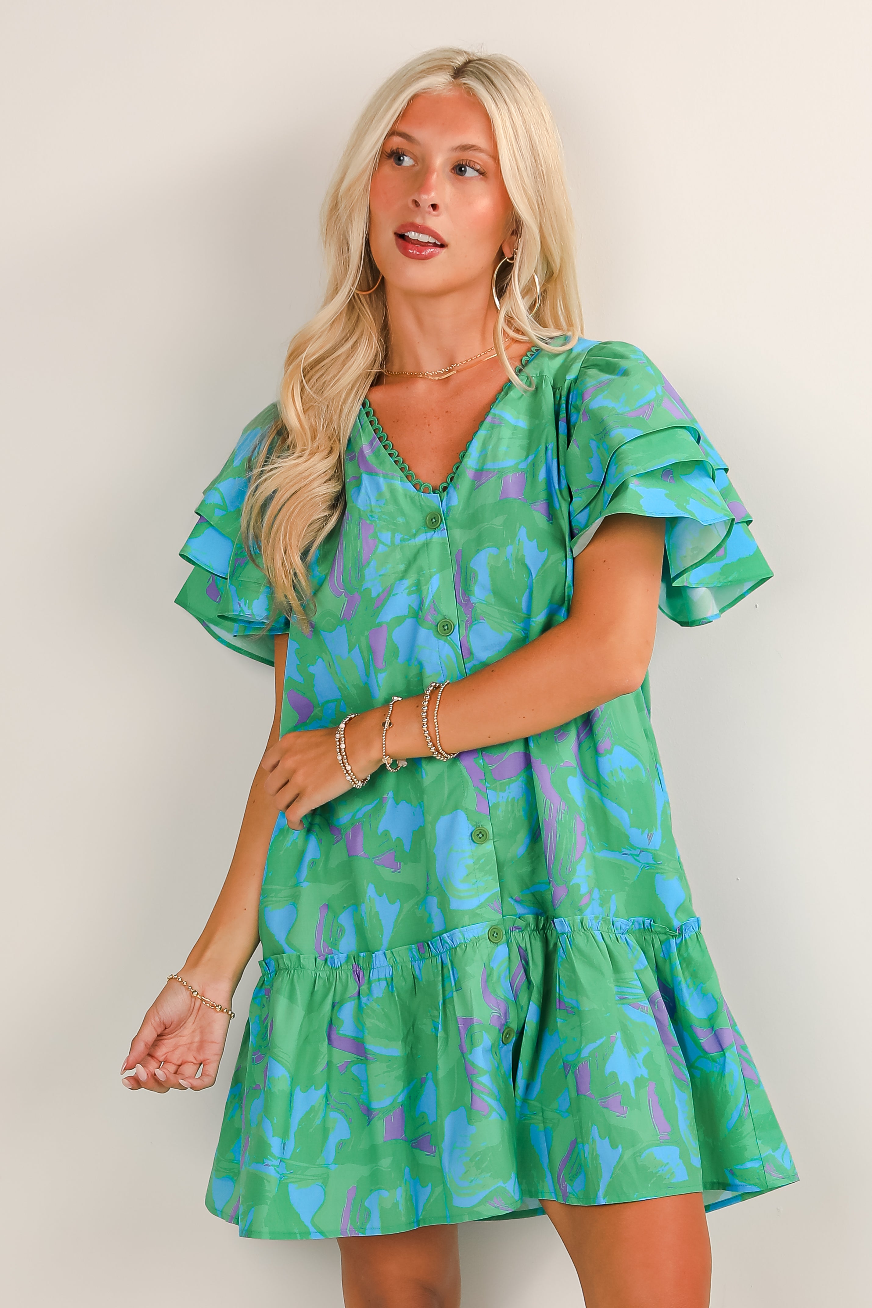 Woman wearing a green dress with blue floral pattern against a plain background