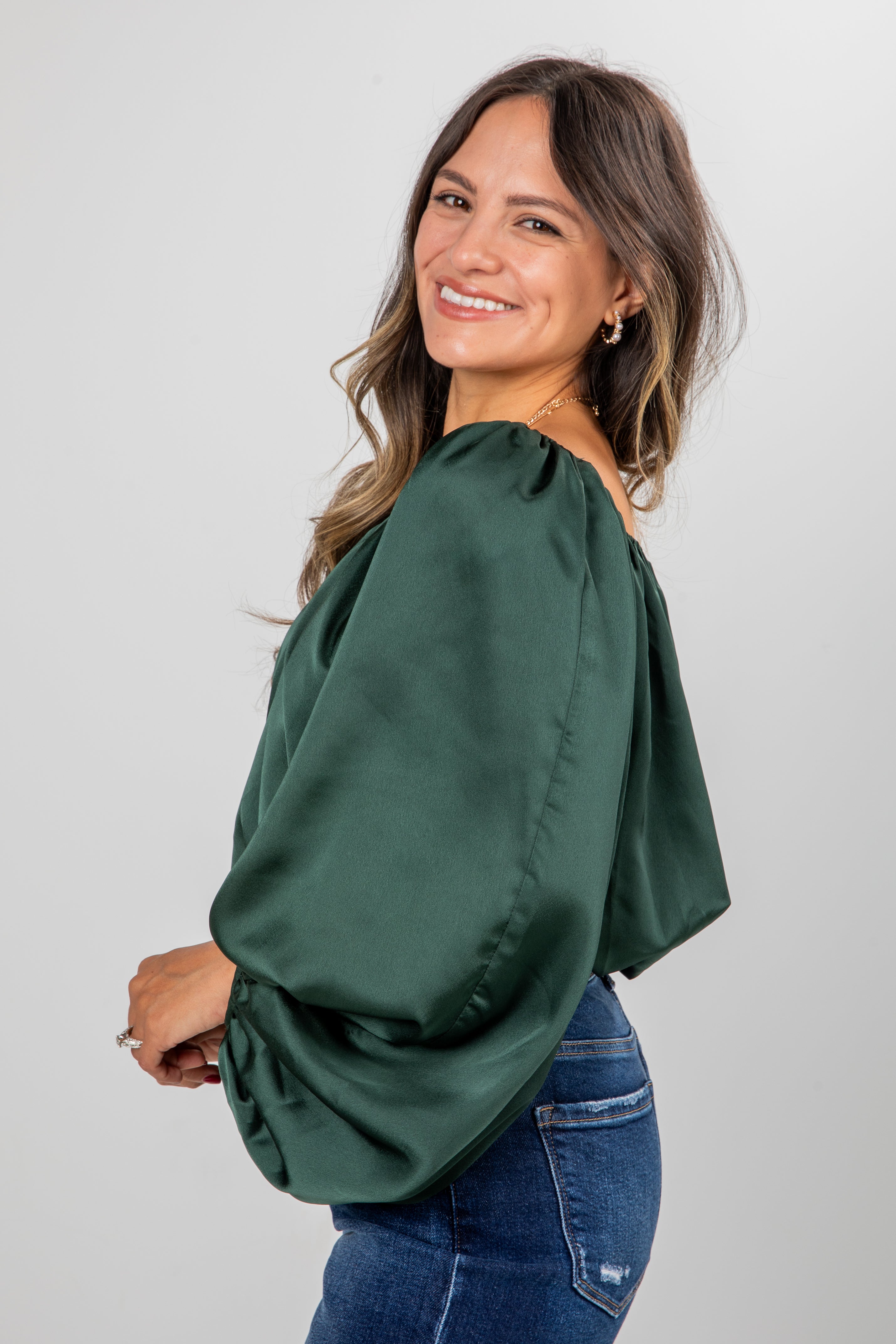 Woman wearing a green blouse and blue jeans against a plain background