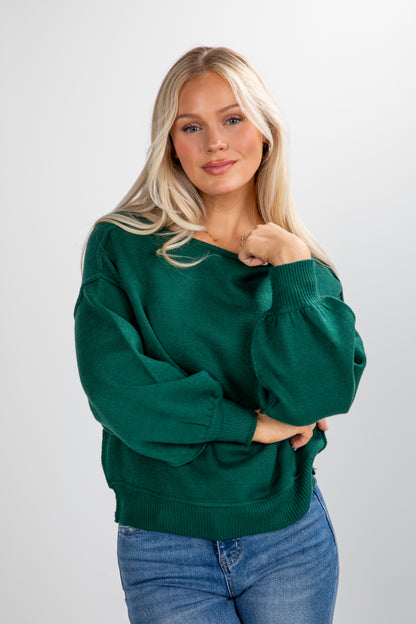 Woman wearing a green sweater and blue jeans on a white background