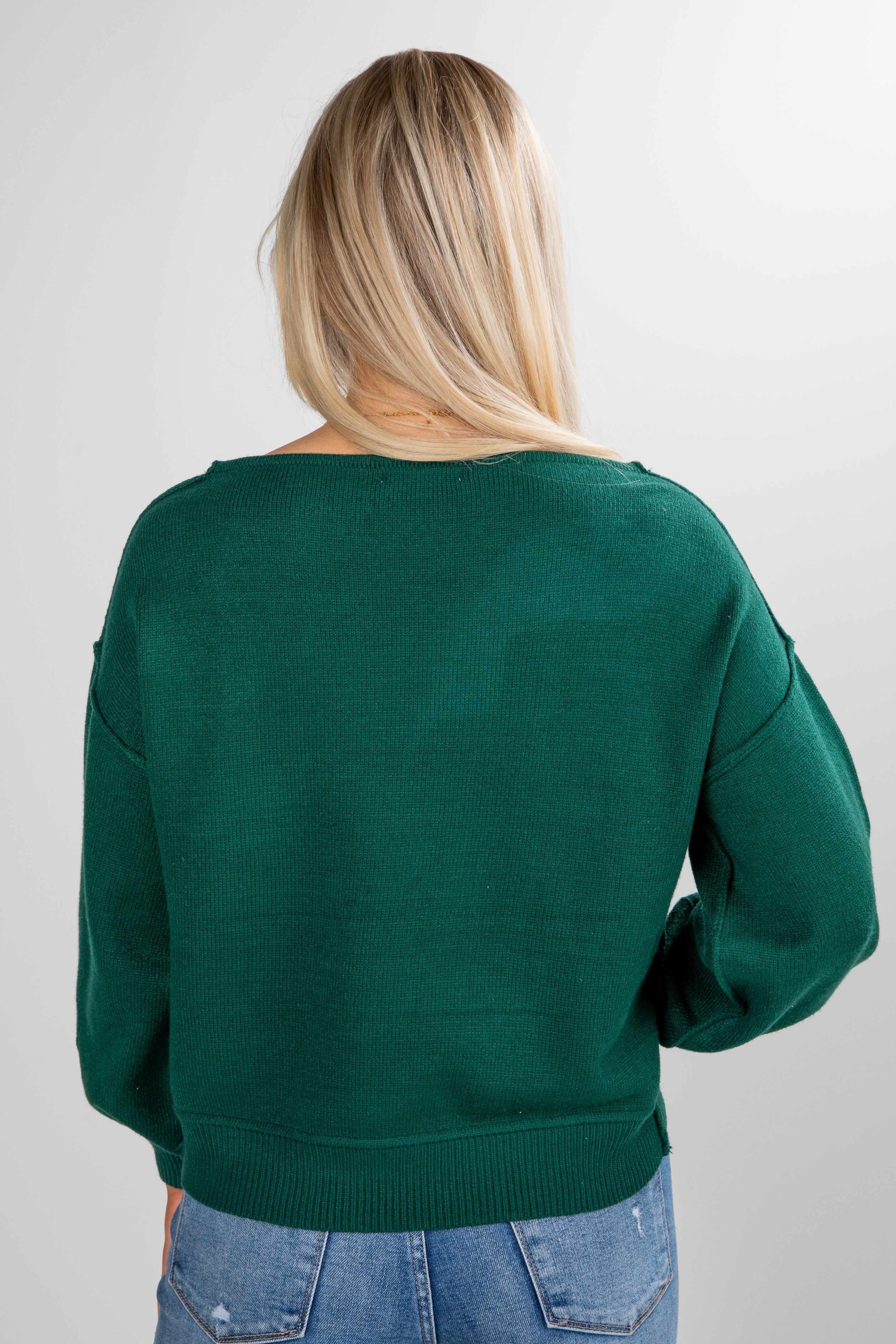 Person wearing a green sweater and blue jeans on a plain background