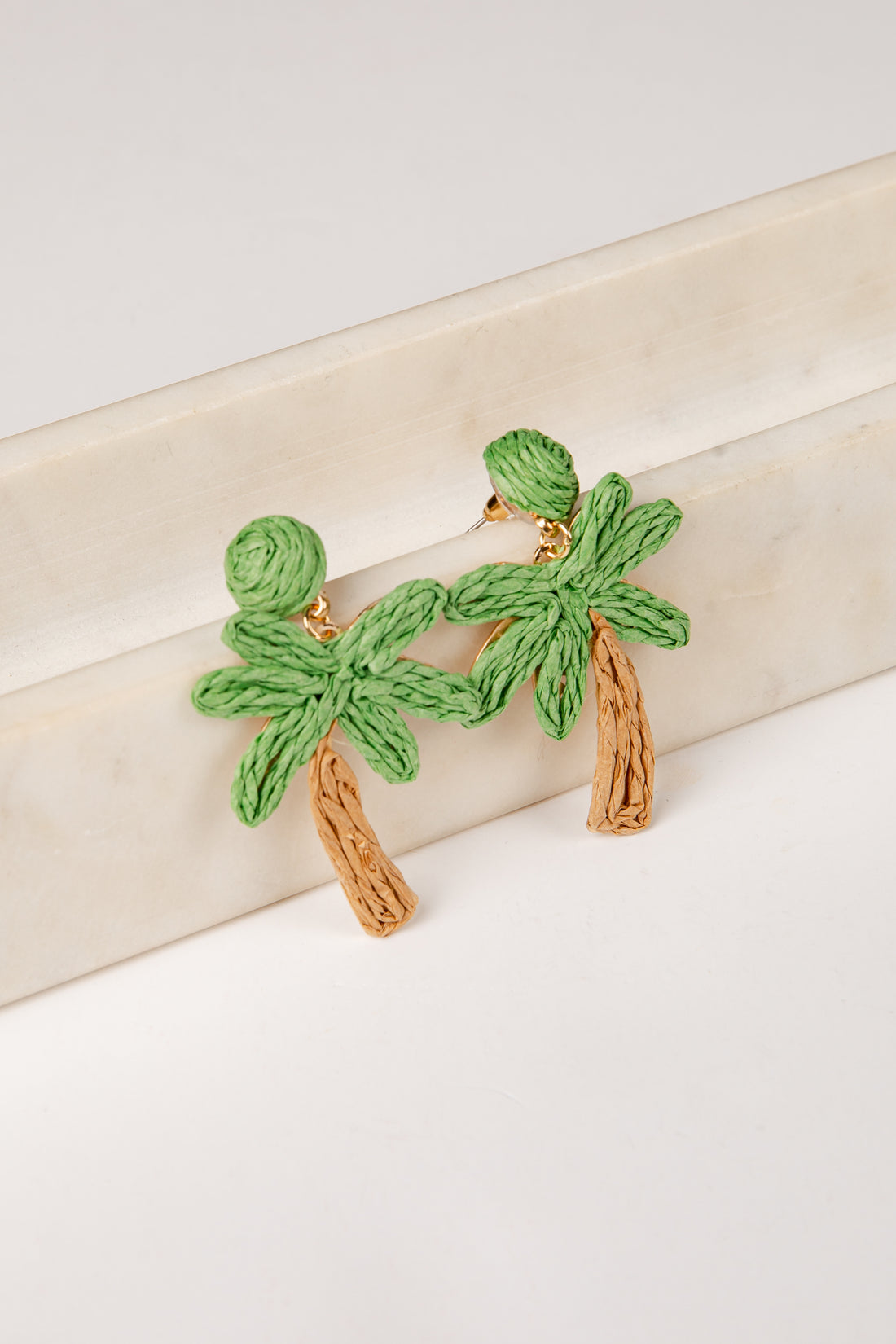 Green palm tree earrings on a beige surface
