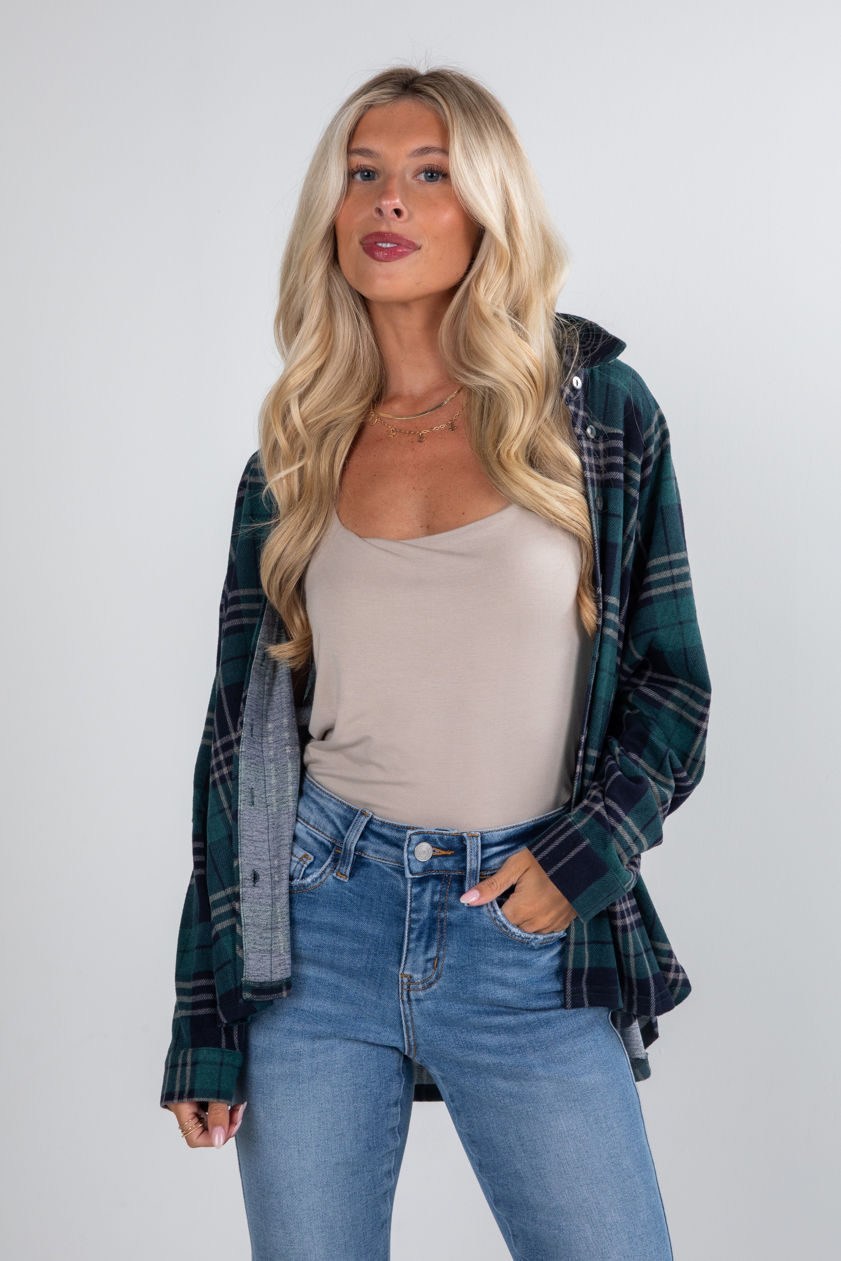 Woman wearing a plaid shirt over a beige top and blue jeans on a white background