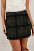 A woman wearing a dark green and black plaid mini skirt with brown and gold intersecting stripes, paired with a white top.