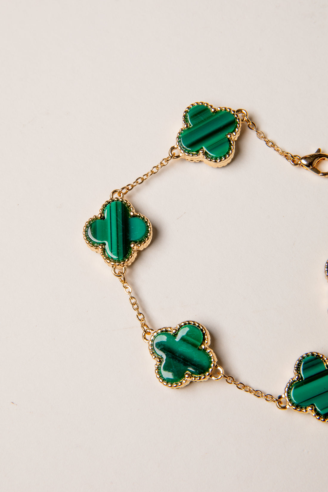 Gold bracelet with green clover-shaped charms on a light background
