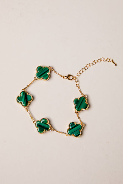 Gold bracelet with green clover-shaped charms on a beige background
