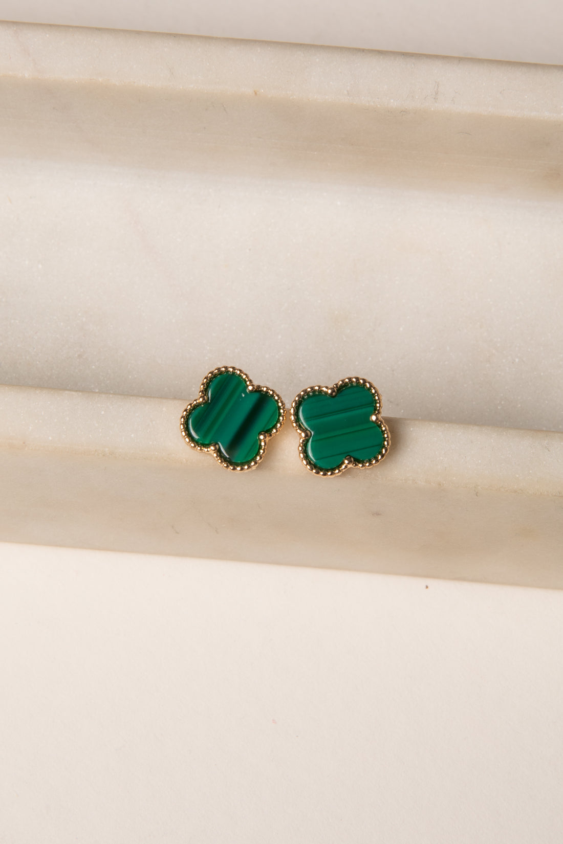 Green clover-shaped earrings on a beige background