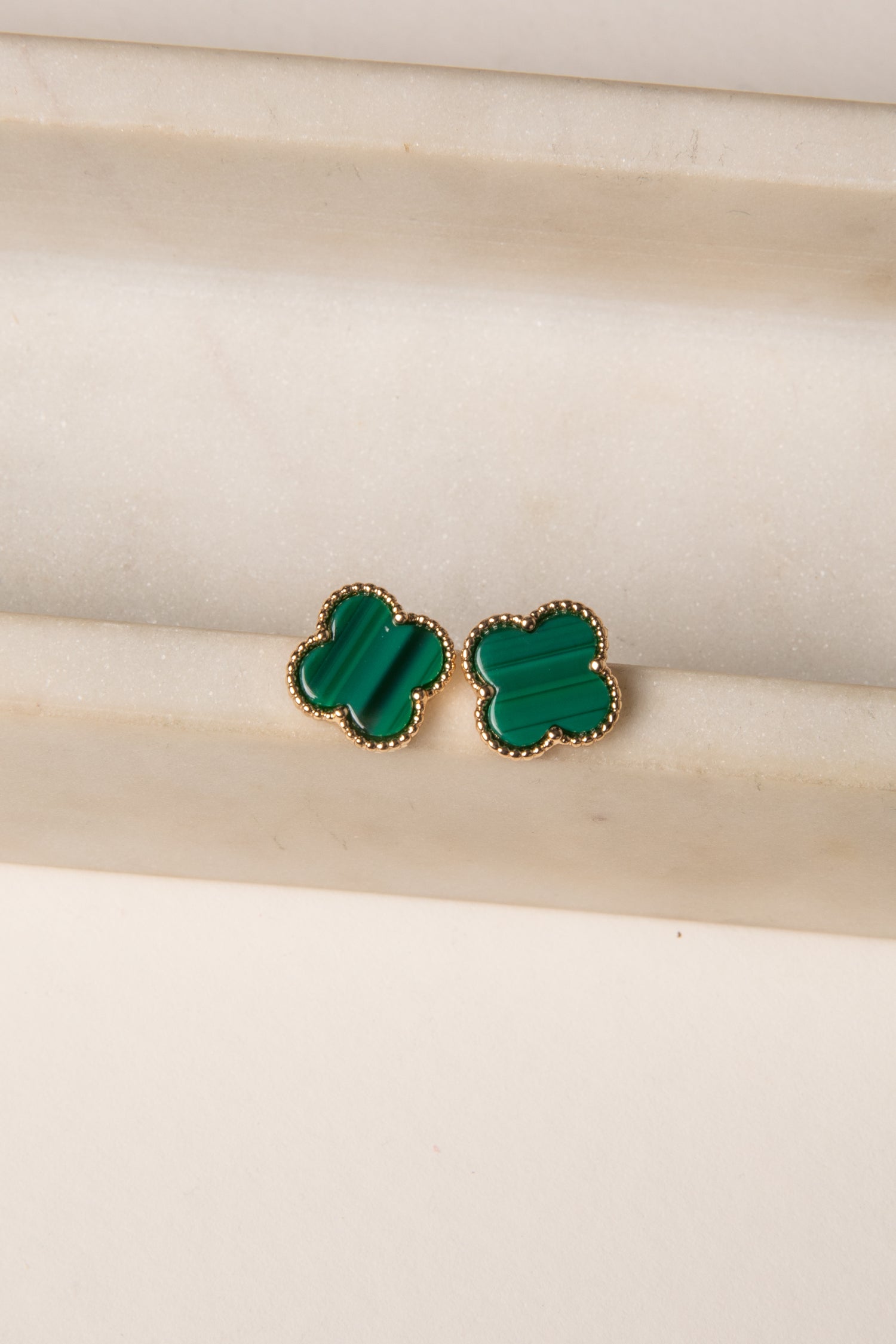 Green clover-shaped earrings on a beige background