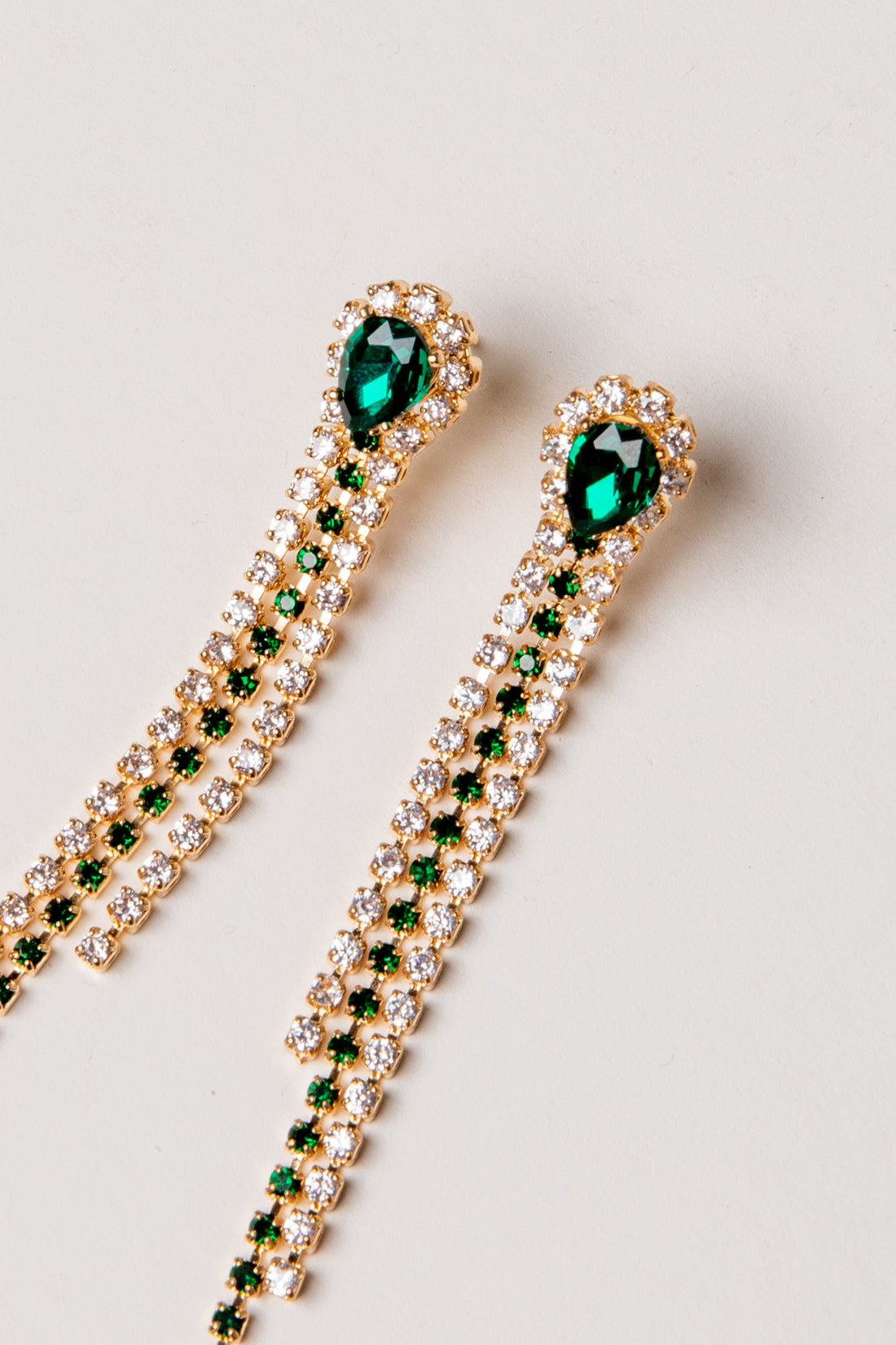 Gold earrings with green gemstones on a light gray background