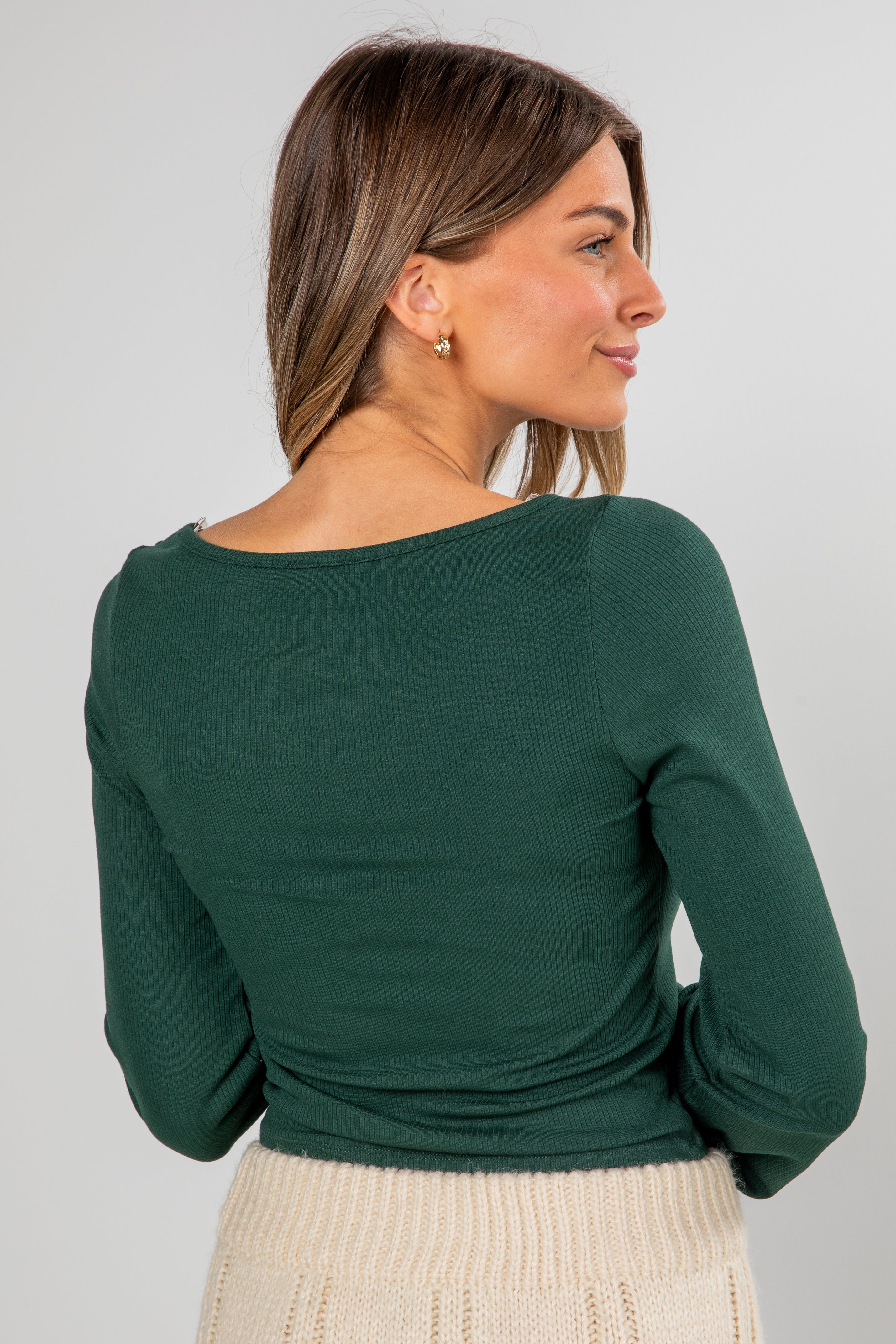 Woman wearing a green long-sleeve top against a gray background