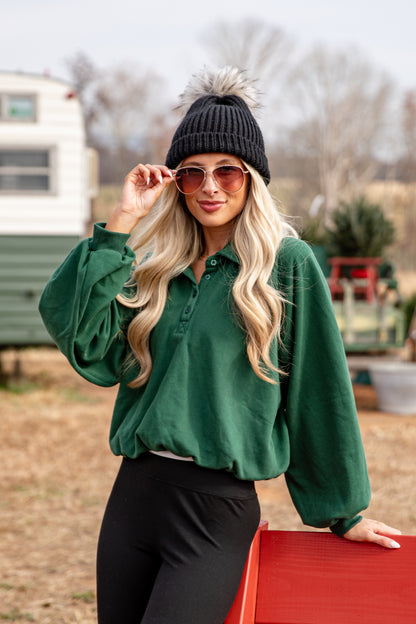Woman wearing a green shirt and black pants standing outdoors with a blurred background